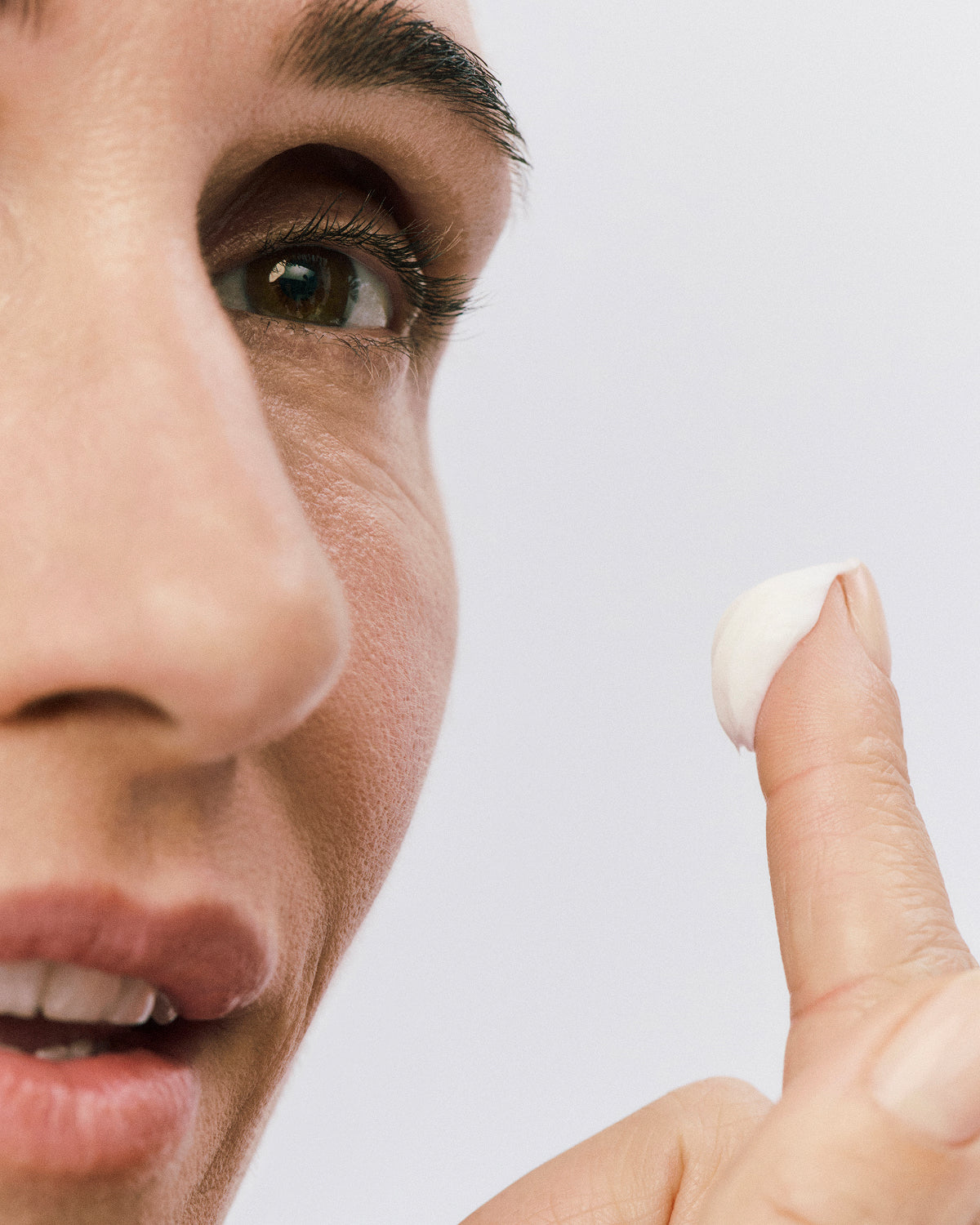 Displays a model in the process of applying a white Counter Cream to her face. 